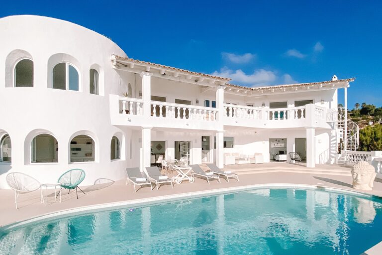 White villa exterior, arched windows, rectangular pool, lounge chairs, balustrade at Villa Penelope, holiday villa in Can Furnet, Ibiza