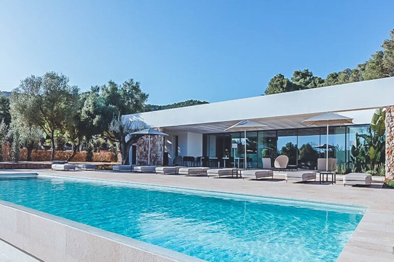 Exterior pool with loungers and modern villa, stone wall and olive trees at Casa Amaya, a luxury villa in San Juan, Ibiza