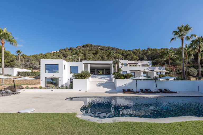 Exterior white villa with curved pool, palm trees, green lawn, sunloungers at Casa Nemo, luxury villa rental in Cap Martinet, Ibiza