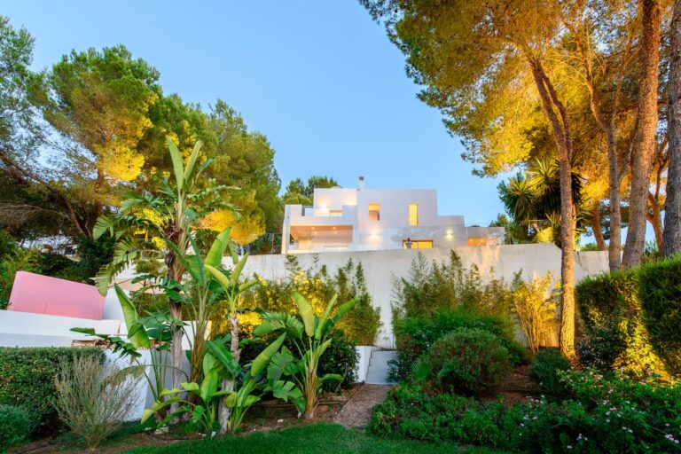 Exterior pool area with loungers and white villa with flowering trees at Eliana Retreat, a luxury villa in San Antonio, Ibiza