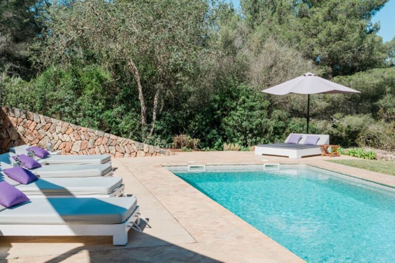 Poolside, white loungers with purple cushions and umbrella, olive trees at Nicole Estate in Santa Eulalia del Rio, Ibiza