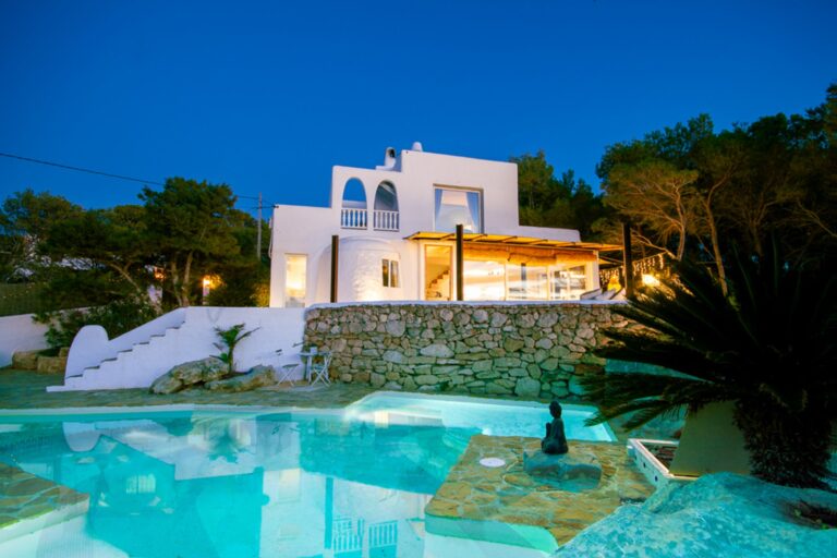 White villa at night with pool and stone retaining wall at Salada Lookout in San Antonio, Ibiza