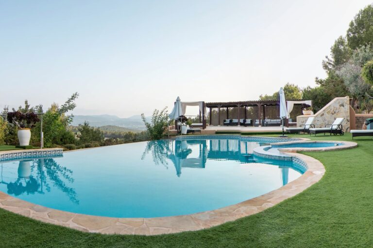 Large pool with lounge chairs, pergola and distant mountains at Yolanda One in San Antonio, Ibiza