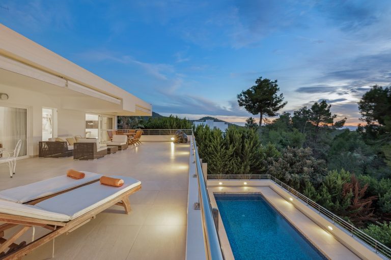 Exterior, terrace lounge at dusk with pool and white furniture at Villa Nirvana, a luxury villa in Can Furnet, Ibiza