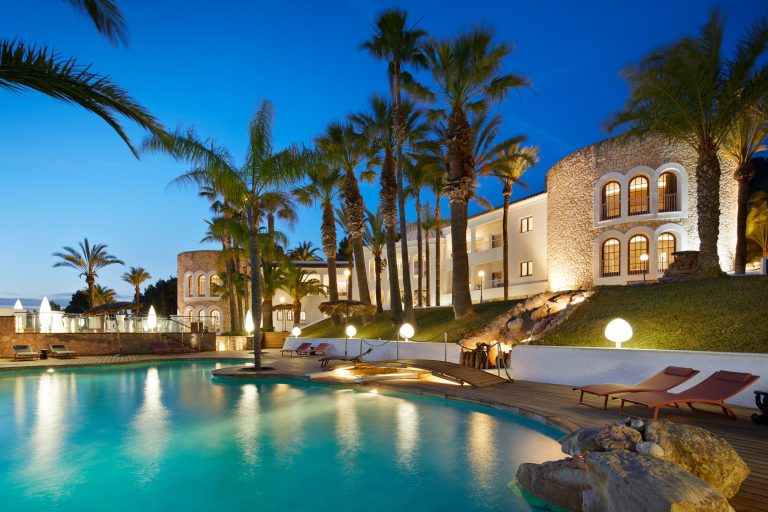 Exterior, illuminated villa with curved turquoise pool at dusk at Villa Amara, villa to rent in Jesus, Ibiza