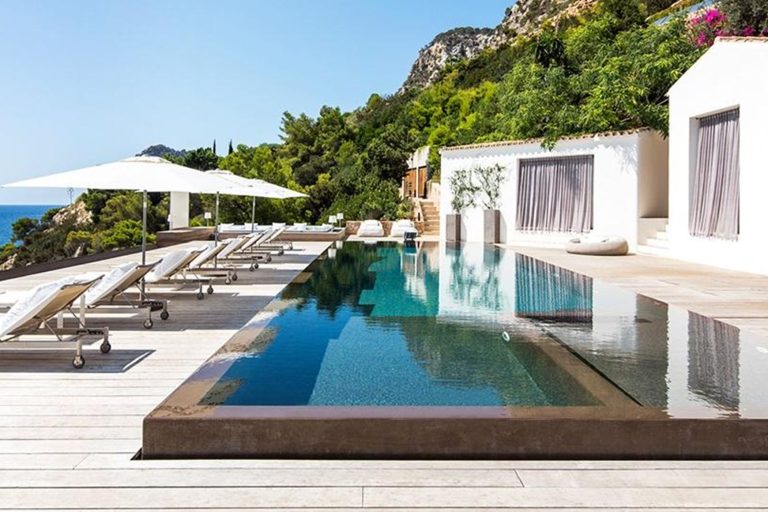 Infinity pool, white villa, wood loungers, sea view, bougainvillea at Villa Baylee, Es Cubells, Ibiza